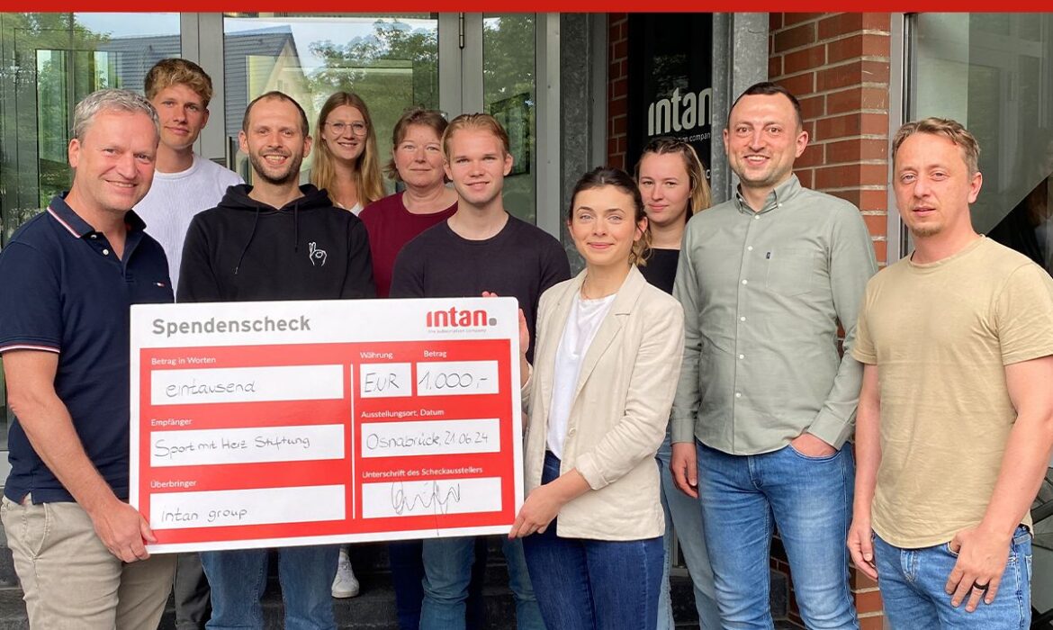 Elf Personen stehen vor dem Eingang eines Bürogebäudes und halten gemeinsam einen großen symbolischen Spendenscheck in der Hand. Der Scheck ist mit dem Logo der intan group versehen und zeigt eine Spende in Höhe von 1.000 Euro an die „Sport mit Herz Stiftung“. Oben im Bild steht in weißer Schrift auf rotem Hintergrund: „intan Bewegungschallenge 2024“.