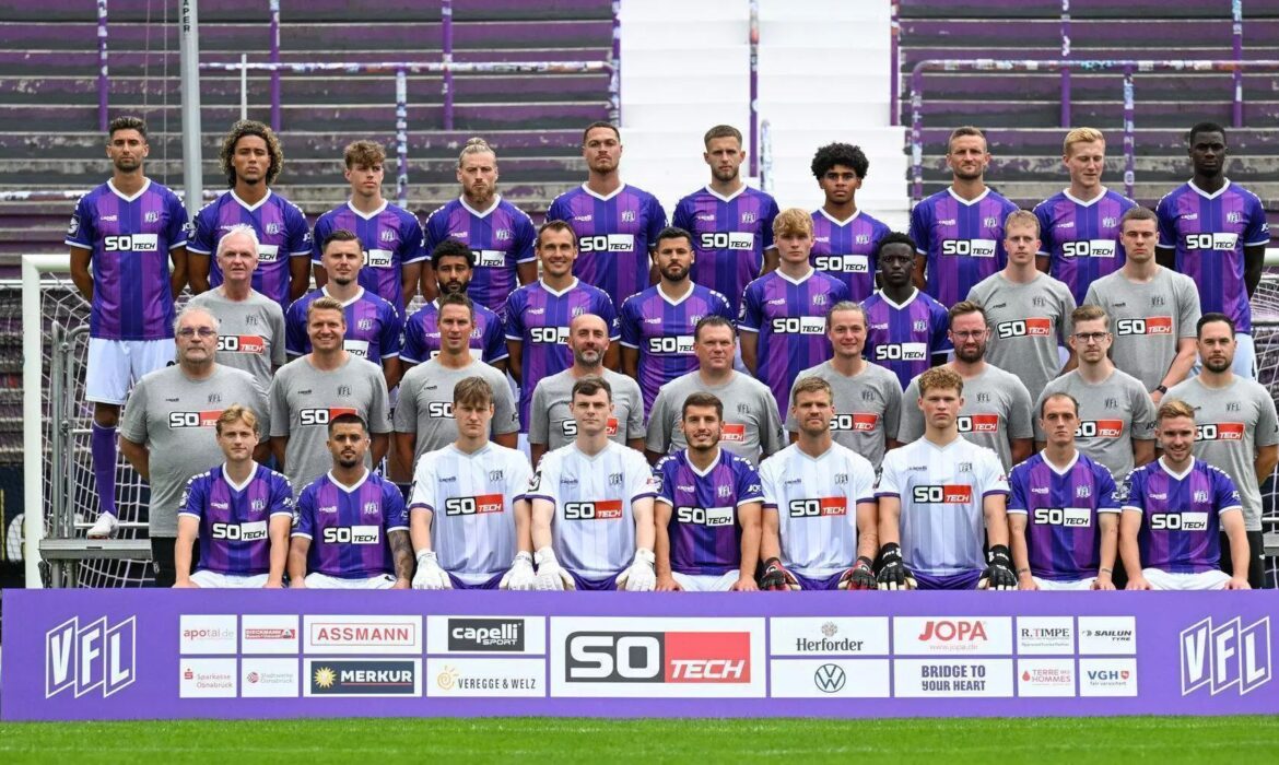 Mannschaftsfoto eines Fußballteams im Stadion. Etwa 35 Personen stehen und sitzen in mehreren Reihen vor leeren Tribünen. Die Spieler tragen überwiegend lila Trikots mit weißen Hosen, einige weiße Trikots. Davor steht eine Werbebande mit Logos und dem VfL-Emblem.