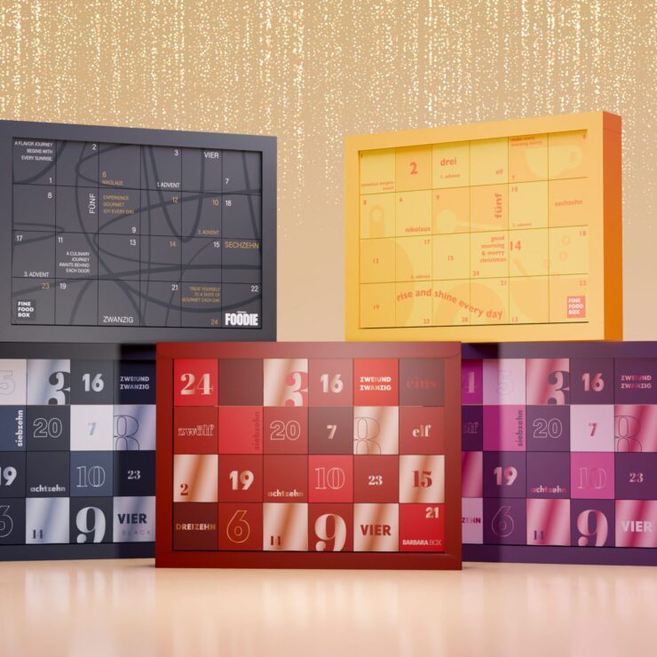 Fünf unterschiedlich gestaltete Adventskalender stehen vor einem gold schimmernden Hintergrund. Jeder Kalender zeigt ein eigenes Design mit Zahlen von 1 bis 24 und verschiedenen Farben wie Dunkelblau, Rot, Violett, Gelb und Grau. Auf einigen sind Markennamen wie „Fine Food Box“, „Foodie“ oder „Barbara Box“ zu erkennen.