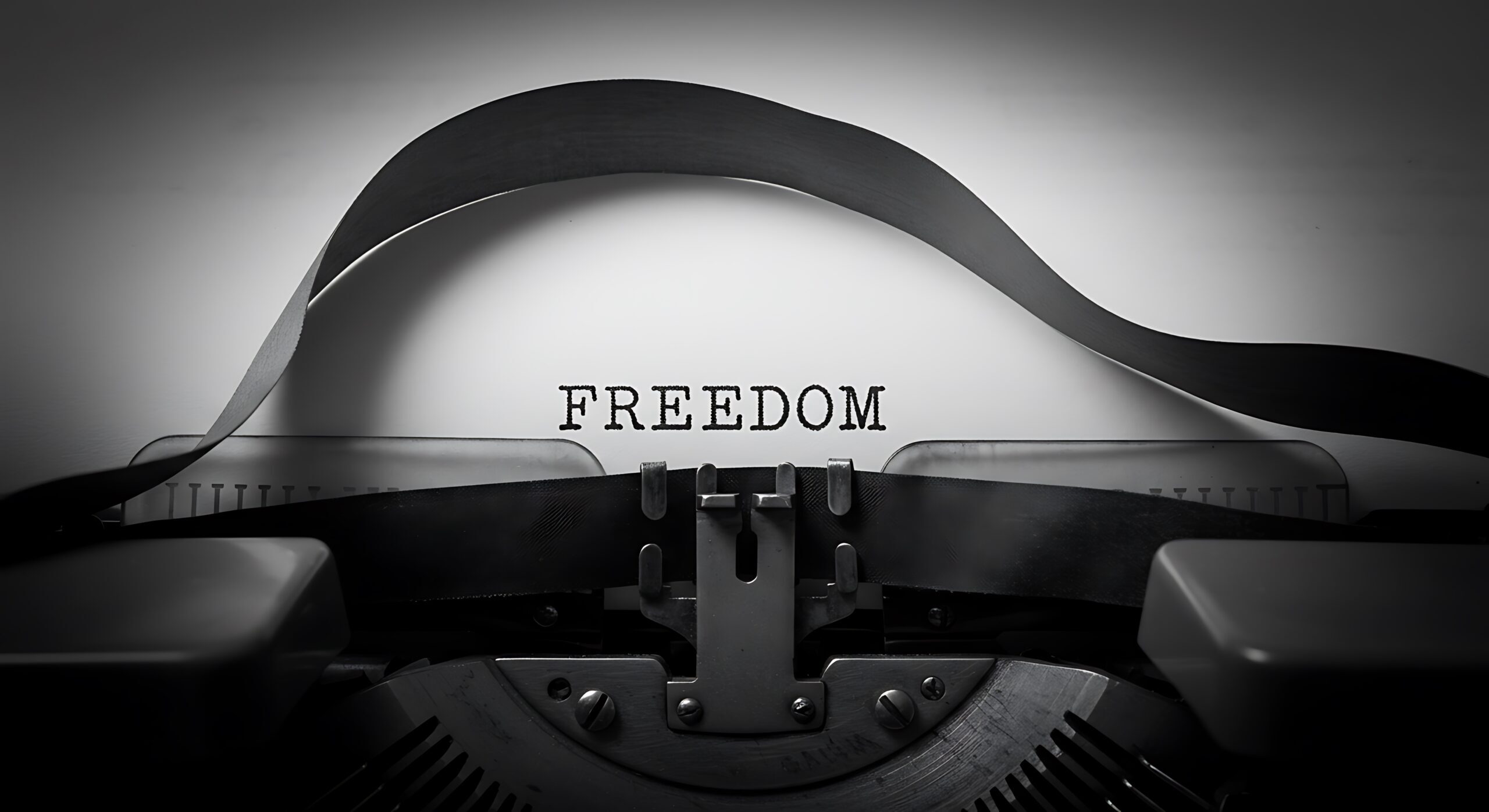 Eine Nahaufnahme einer Schreibmaschine, auf deren Papier das Wort „FREEDOM“ in Großbuchstaben getippt ist. Das Bild ist in Schwarz-Weiß gehalten und wirkt symbolisch und kontrastreich.