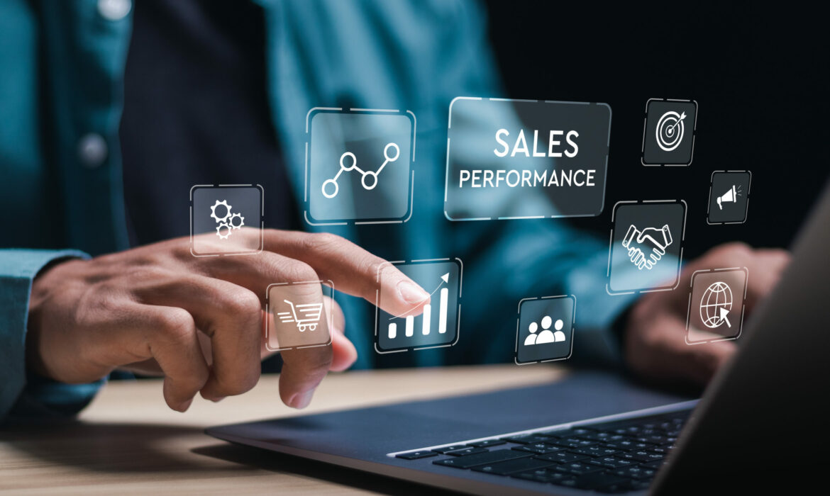 Das Bild zeigt eine Person, die an einem Laptop arbeitet und mit dem Finger auf digitale Symbole tippt, die virtuell über dem Gerät eingeblendet sind. Zu sehen sind grafische Icons wie ein Einkaufswagen, ein Balkendiagramm, Zahnräder, ein Netzwerk, eine Zielscheibe, ein Handschlag und weitere Symbole. Im Zentrum der Darstellung steht der Schriftzug „SALES PERFORMANCE“. Die Szene vermittelt ein modernes, digitales Arbeitsumfeld im Bereich Vertrieb und Performance-Analyse.