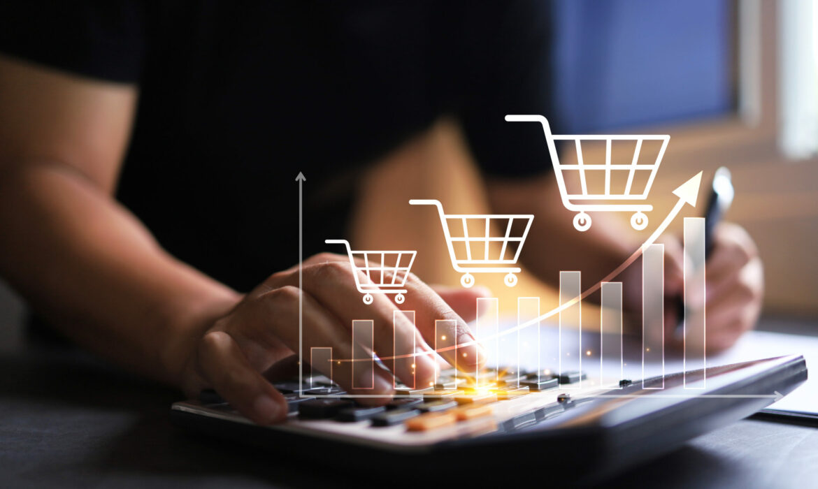 Das Bild zeigt eine symbolische Darstellung von wachsendem Verkaufserfolg. Eine Person tippt auf einen Taschenrechner, während darüber eine grafische Kurve mit aufsteigenden Balken und Einkaufswagen-Symbolen eingeblendet ist. Die Visualisierung steht für Umsatzwachstum, E-Commerce oder eine Verkaufsanalyse – der steigende Verlauf der Symbole signalisiert positive Entwicklung und Erfolg im Vertrieb. Es handelt sich um ein starkes Motiv für Themen wie Sales, Business Development oder Onlinehandel.