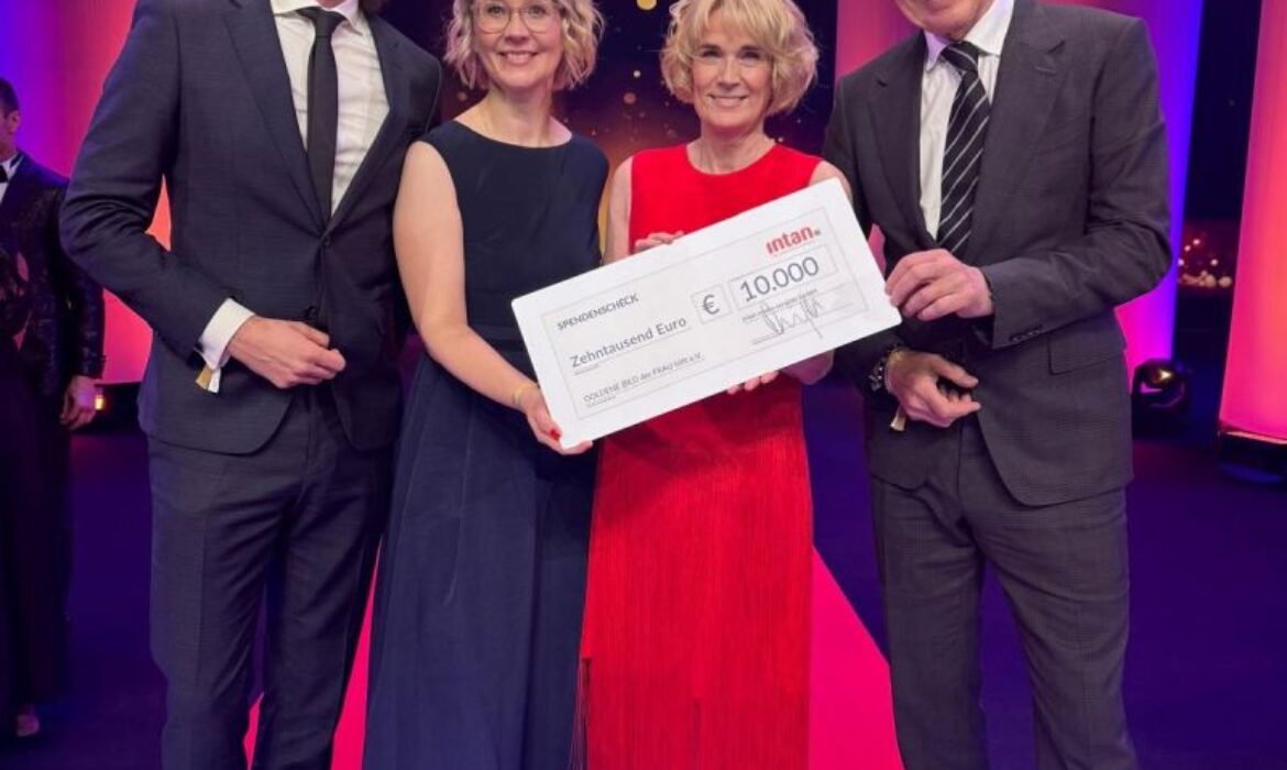 Vier festlich gekleidete Personen stehen auf einer Bühne bei der Preisverleihung „Die Goldene Bild der Frau 2024“. Sie halten gemeinsam einen großen symbolischen Spendenscheck der intan group über 10.000 Euro. Im Hintergrund leuchten pinke und goldene Lichteffekte, auf der Bühne ist das Logo der Veranstaltung zu sehen.