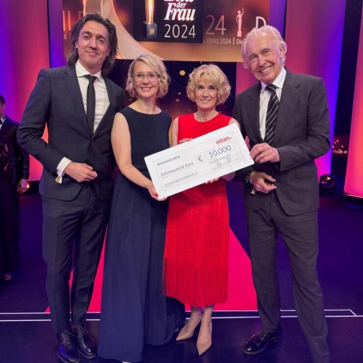 Vier festlich gekleidete Personen stehen auf einer Bühne bei der Preisverleihung „Die Goldene Bild der Frau 2024“. Sie halten gemeinsam einen großen symbolischen Spendenscheck der intan group über 10.000 Euro. Im Hintergrund leuchten pinke und goldene Lichteffekte, auf der Bühne ist das Logo der Veranstaltung zu sehen.