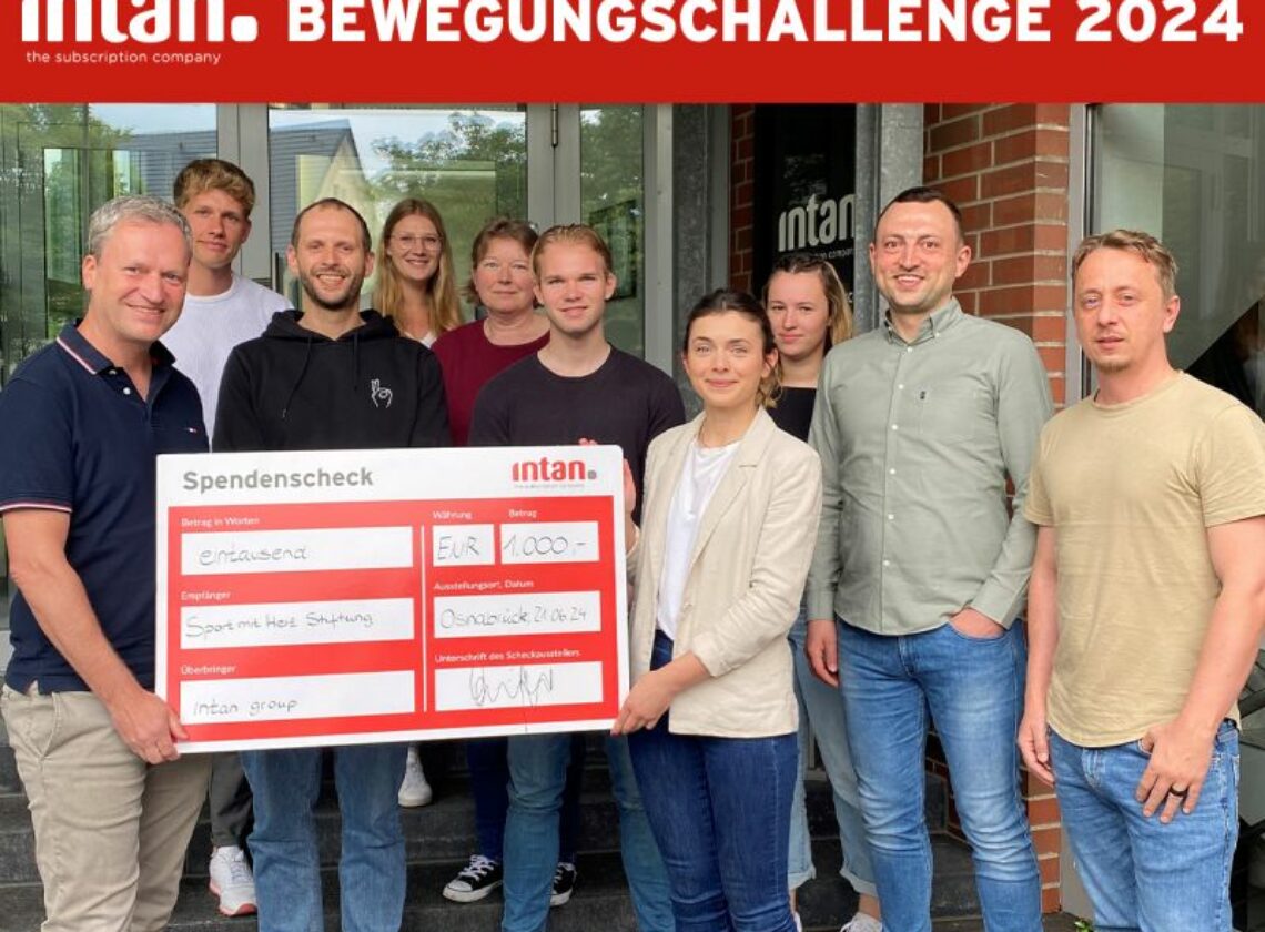 Elf Personen stehen vor dem Eingang eines Bürogebäudes und halten gemeinsam einen großen symbolischen Spendenscheck in der Hand. Der Scheck ist mit dem Logo der intan group versehen und zeigt eine Spende in Höhe von 1.000 Euro an die „Sport mit Herz Stiftung“. Oben im Bild steht in weißer Schrift auf rotem Hintergrund: „intan Bewegungschallenge 2024“.