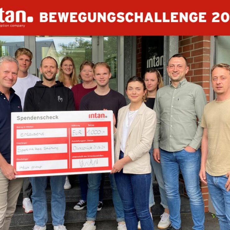 Elf Personen stehen vor dem Eingang eines Bürogebäudes und halten gemeinsam einen großen symbolischen Spendenscheck in der Hand. Der Scheck ist mit dem Logo der intan group versehen und zeigt eine Spende in Höhe von 1.000 Euro an die „Sport mit Herz Stiftung“. Oben im Bild steht in weißer Schrift auf rotem Hintergrund: „intan Bewegungschallenge 2024“.