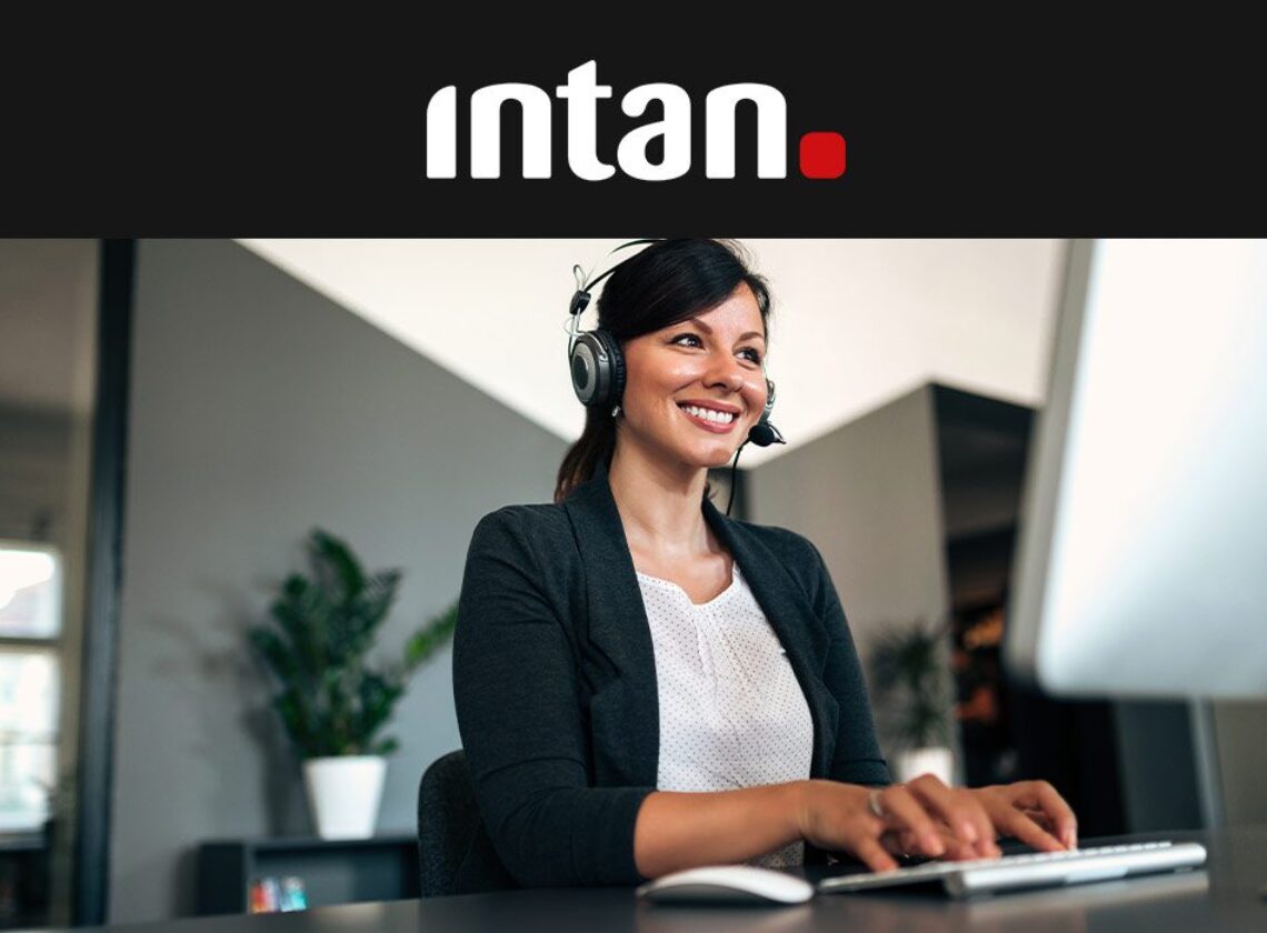 Frau sitzt laechelnd am PC und telefoniert via Headset