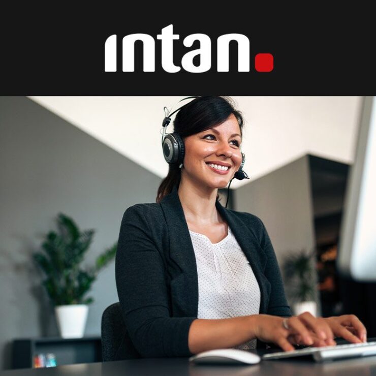 Frau sitzt laechelnd am PC und telefoniert via Headset