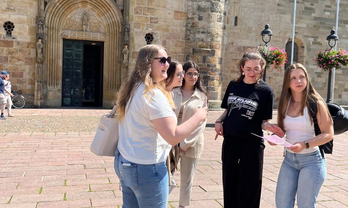 Vier junge Frauen, aktuelle intan Auszubildende 2025, vor dem Osnabrücker Dom. Sie halten eine Karte der Stadtralley in den Händen und sind in Bewegung und im Gespräch.