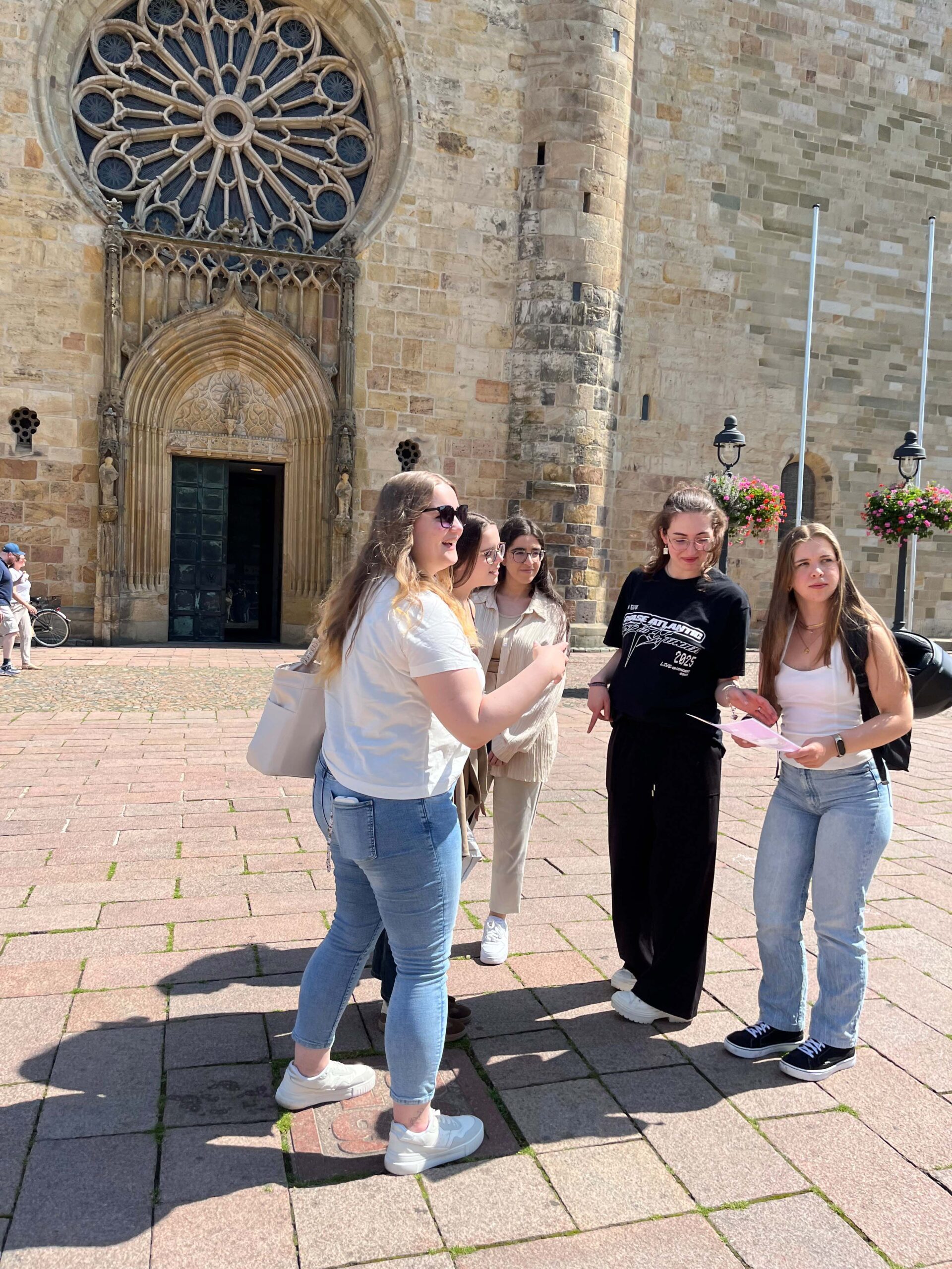 Vier junge Frauen, aktuelle intan Auszubildende 2025, vor dem Osnabrücker Dom. Sie halten eine Karte der Stadtralley in den Händen und sind in Bewegung und im Gespräch.